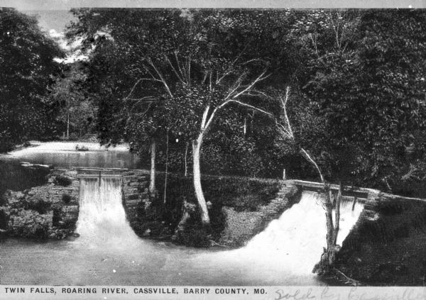 Twin waterfalls on Roaring river flowing over weathered stonewalls with river and forest in the background. Caption reads "Twin Falls, Roaring River. Cassville, Barry County."