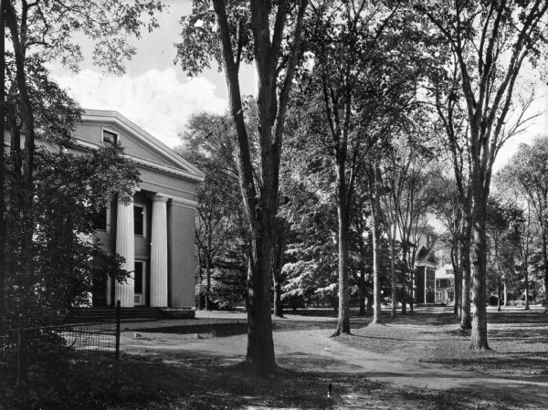 Front of town hall built in classical style with two-story columns.  In front of the building is a large lawn with two rows of trees.  In the background, more trees and other large buildings are visible.