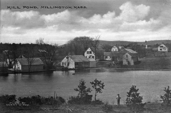 Elevated view of mill pond and homes along the opposite shoreline. A person is standing at the shoreline in the foreground. Caption reads, "Mill Pond, Millington, Mass."