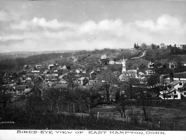 Elevated view from hill toward town, including houses, a church and surrounding wooded hills. Caption reads, "Bird's-eye View of East Hampton, Conn."