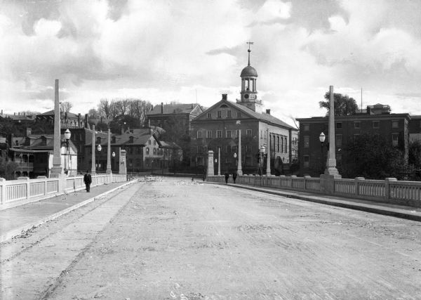 Street-level view of the Central Moravian Church from an adjacent bridge lined with stone balustrades and wide sidewalks. A work crew is at the intersection. Other large buildings flank the church in the background.