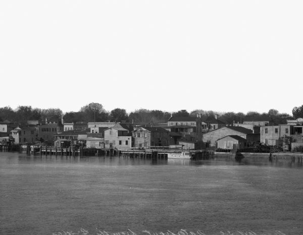 The Beaufort river waterfront as seen from Lady's Island bridge. There are wooden buildings, piers and a tree-line in the background.
