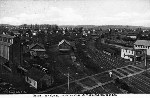 Elevated view of a train yard with six sets of railroad tracks and large wooden buildings. A nearby neighborhood is visible in the background. Caption reads: "Bird's-eye view of Ashland, Ohio."