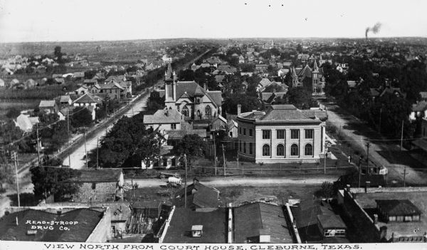 Elevated view looking north from the courthouse onto the center of town with two large stone buildings in the foreground and residential neighborhoods stretching into the distance. Caption reads, "View North from Court House, Cleburne, Texas."