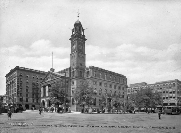 A view from the street of the Courthouse with a stone monument in front. Other large buildings are next to the Courthouse, and pedestrians are on the sidewalk. Caption reads: "Public Square and Stark County Courthouse, Canton, Ohio."