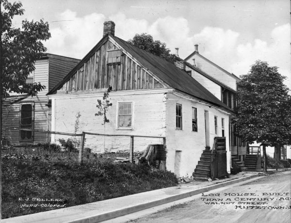 Angled view from street toward a log house on Walnut Street. Caption reads: "Log House, Built [More] Than A Century Ag[o], Walnut Street. Kutztown, PA."