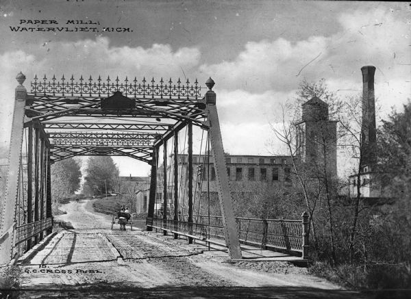 View from other side of bridge toward the paper mill, with a bridge and road to the left. A horse-drawn vehicle is on the bridge. Caption reads: "Paper Mill, Watervliet, Mich."