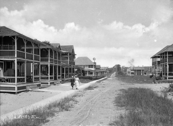 A view of homes on Swan Avenue. Most prominent are the screened porches that cover the facade of the homes. Two women are walingk down the sidewalk toward the viewer.
