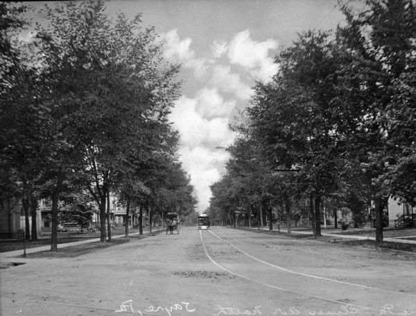 View down Elmer Avenue, taken from the middle of the street. A street car and carriage are moving along the street; the car moves away from the camera, and the carriage moves toward the camera. Trees line the terrace, partially obscuring the houses.