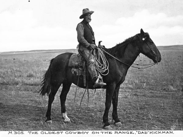 Outdoor portrait of Dad Hickman who is sitting on a horse in a field.  Hickman is looking at the camera and is wearing a plaid shirt. He has a rope coiled up on the saddle. Caption reads: "The Oldest Cowboy on the Range, 'Dad' Hickman."
