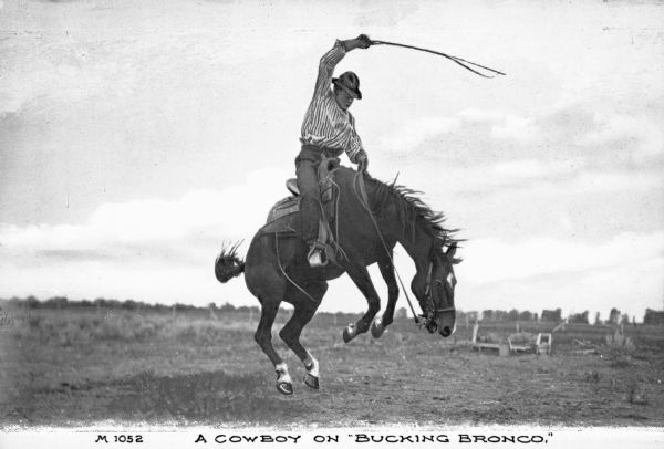 Ranch hand holding a crop high above his head on a bucking horse. In the distance are trees and shrubs. Caption reads: "'A Cowboy on Bucking Bronco.'"