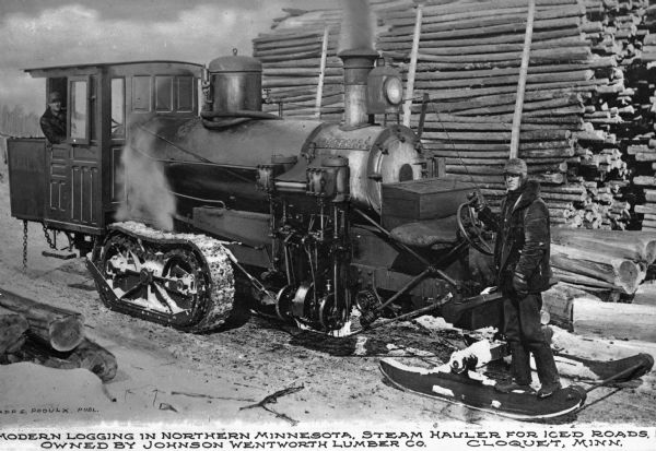 A view of a steam hauler used for pulling logs. A man is standing inside of the hauler with his head out of the window. On the right a man is standing in front of the machine near the steering wheel, and behind him is a large pile of logs. Caption reads: "Modern Logging in Northern Minnesota. Steam Hauler for Iced Roads, Owned by Johnson Wentworth Lumber Co. Cloquet, Minn."

The Johnson Wentworth Lumber company was founded in 1894 by Samuel S. Johnson, parts of the company sold to both The Cloquet Lumber Company and The Northern Lumber Company in 1902.
