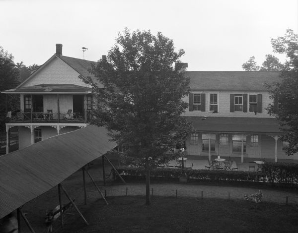Elevated view of the house, with the covered walkway on the left. Chairs are on the second floor porch of the house.