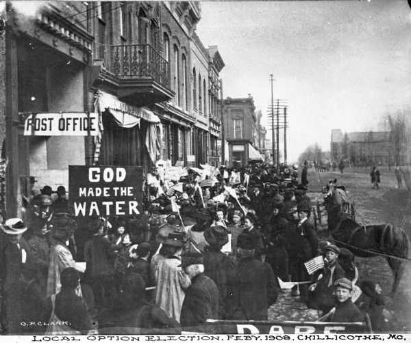 A view of the crowds at an election. The crowd, mostly women, stand in front of the post office. A sign says "God Made the Water." Printed below the image: "Local Option Election, Feb'y. 1908, Chillicothe, MO."