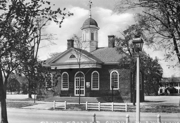 View across street toward the colonial court house. The brick structure has a cupola on the roof with a weather vane.