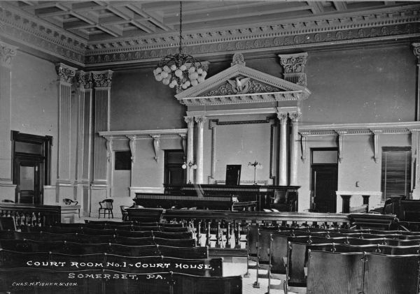 A view of the interior, focusing on the judge's chair. The room has many classical decorative details, reminiscent of the Federal Style popular shortly after the Revolutionary War. Caption reads: "Court Room No. 1 — Court House, Somerset, PA."