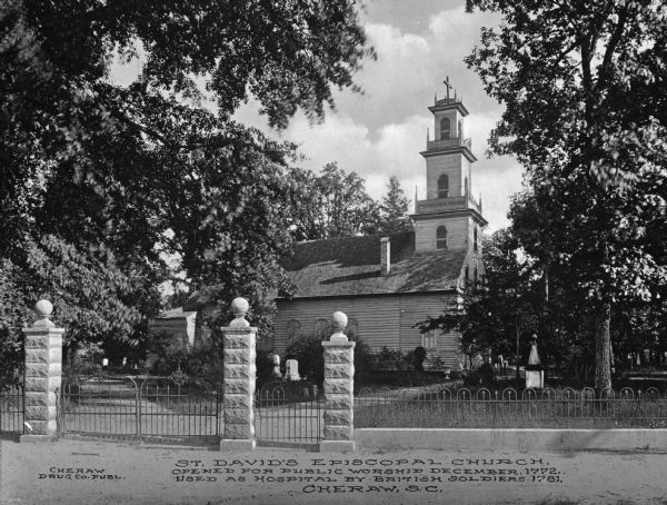A view of the church from the side, as well as a view of the grounds, which includes a cemetery. An iron fence surrounds the grounds, with both carriage and regular entrances. Caption reads: "St. David's Episcopal Church, Opened for Public Worship December, 1772. Used As Hospital for British Soldiers 1781.  Cheraw, S. C."
