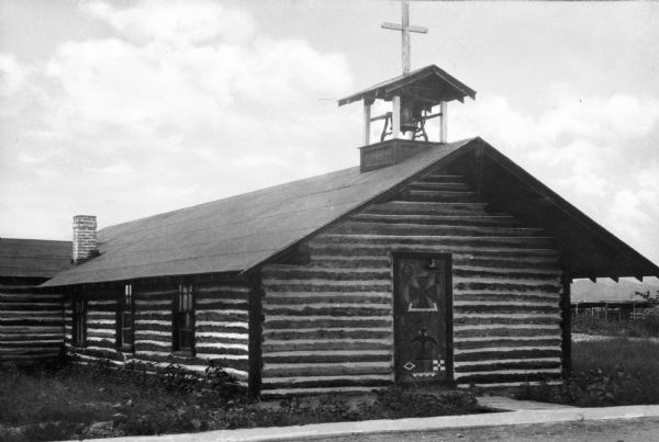 A view of the log church, with steeple and bell tower. The front door is painted with symbols.