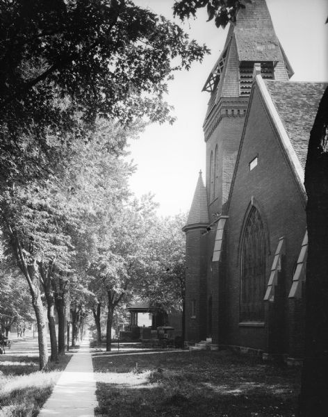 View down sidewalk with a church on the right. There is a large arched stained glass window on the front.