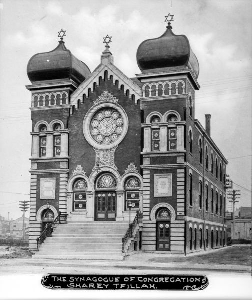 A view of the synagogue's facade and right side. The building has a combination of brick and stone, with horseshoe arches above doors and windows. The windows are multi-paned and have stained glass. The towers have onion domes. Caption reads: "The Synagogue of Congregation Sharey Tfillah."