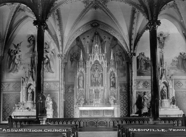 View from aisle toward the main and side altars of the Assumption Church. Murals decorate the walls and the  main altar contains four statues and a mural of the crucifix. The left side altar is devoted to Mary, with statues of her on and beside the altar. The right side altar is devoted to Jesus, with statues of him on and beside the altar. Caption reads: "Assumption Church, Nashville, Tenn."