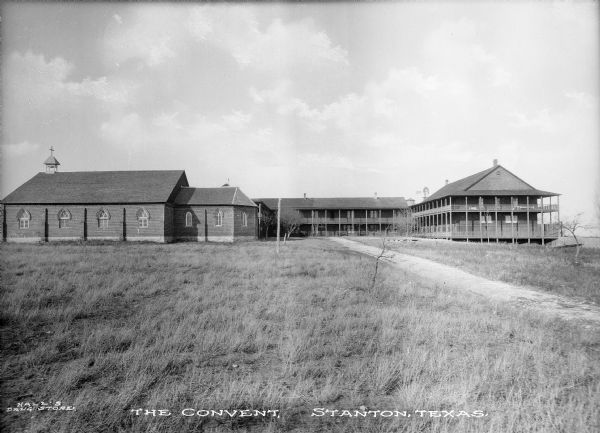 View across field of grass toward the convent. The chapel is at the left, and there is an L-shaped housing structure, with porches on the first and second levels, in the center and on the right. Caption reads: "The Convent, Stanton, Texas."