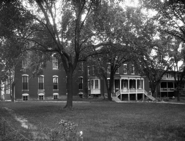 Westminster College building surrounded by a lawn and trees. The building is made of brick and has a large porch at the main entrance with two sets of steps leading to it. Another building stands to the right.