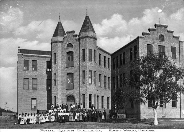 Outdoor group portrait of African American students posing in front of a large brick building. Two turrets flank the arched main entrance, with wings jutting off on both sides. Caption reads: "Paul Quinn College, East Waco, Texas."