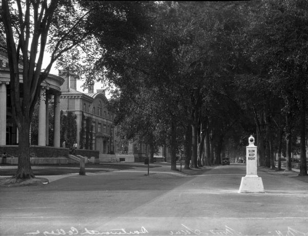 A view of the street that runs through the Dartmouth College campus.  Trees and buildings line the way, with a stone "Slow Keep Right" obelisk in the middle of the road.