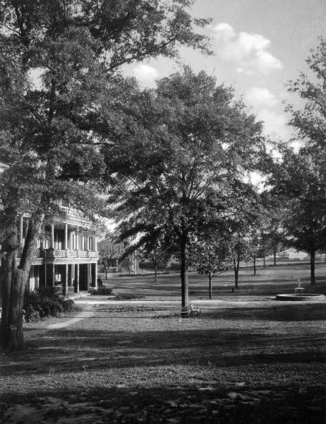 A view of the green space and buildings on the campus of Bessie Tift College. Trees stand near the buildings and a fountain is to the right.
