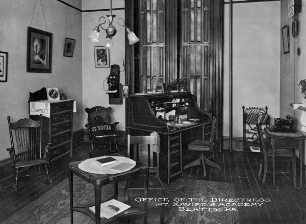 A view of the Office of the Directress at St. Xavier's Academy. A roll top desk sits by the window and a small table holding a typewriter stands to the right. To the left of the wall is a telephone and chairs sit against the wall. Caption reads: "Office of the Directress, St. Xavier's Academy, Beatty, PA."