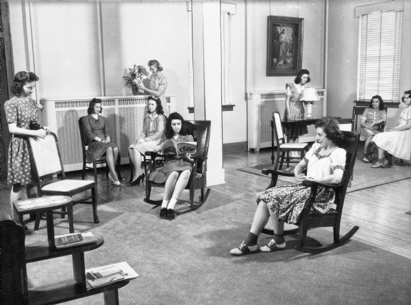 A view of female students relaxing in the reception room at Holy Family Academy. Some sit in groups while others read magazines. Furnishings consist mainly of minimally-upholstered chairs.