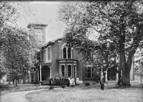 Male and female students pose for a group portrait, with their teacher standing at right, in front of Banneker High School. The structure is made of brick and has two porches and a bell tower.