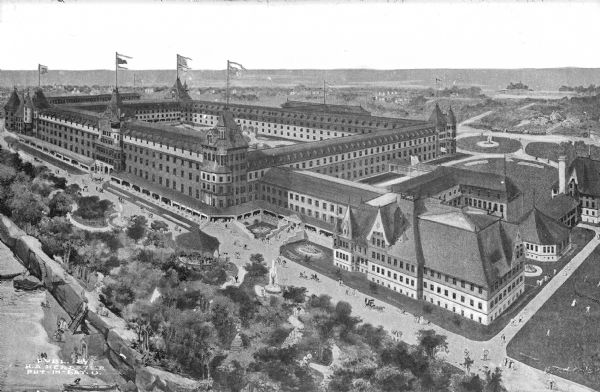 Elevated view of Hotel Victory. The hotel has an inner courtyard, towers, and flags flying on top of the towers. People are milling around the building and strolling along a lake or river on the left.