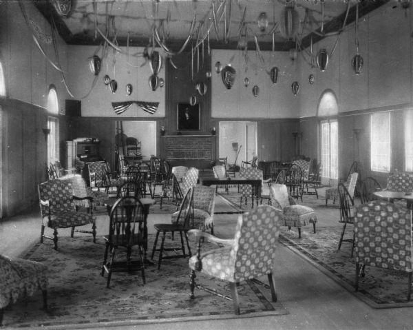 A view of an interior at The Club House, furnished with upholstered and wooden chairs, tables, and rugs. Lanterns and streamers hang the ceiling.