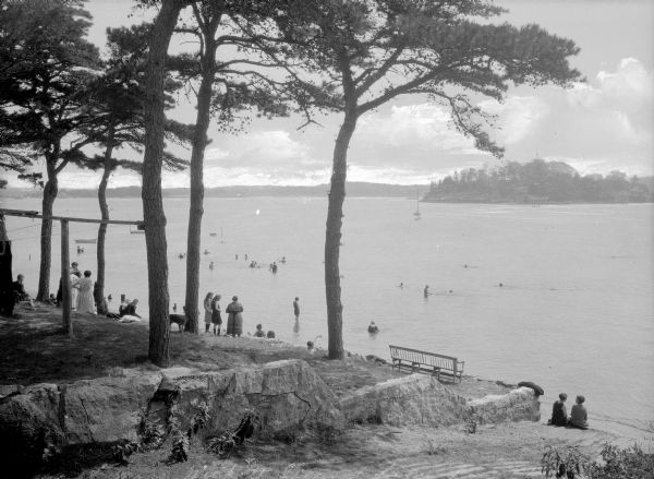 Elevated view of people sunbathing and relaxing on the beach at Wickett Island, while others wade in the lake.