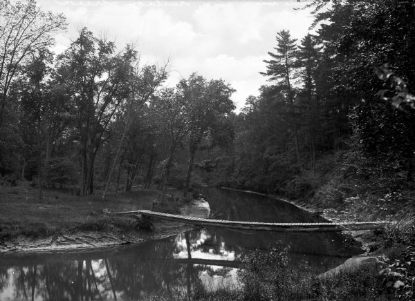 A wooden footbridge crosses Wilson Creek in a wooded area.