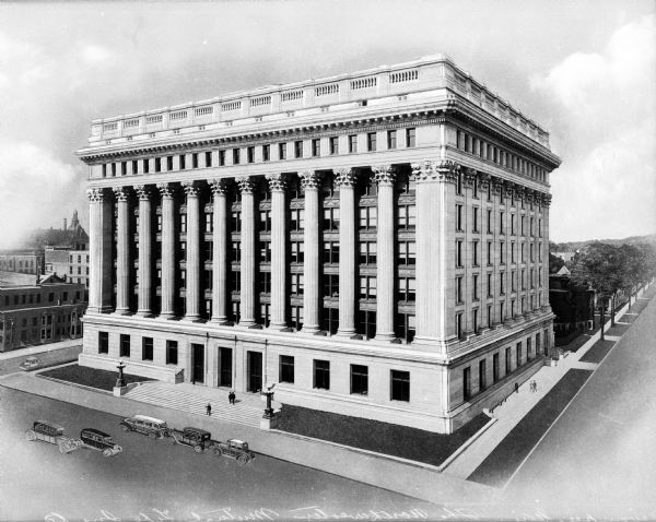 Elevated, angled view of the facade and right side of the Northwestern Mutual Life Insurance Company building. The structure has a set of stone steps that lead from the sidewalk to the ground floor, and the facade has columns that run the length of five stories.
