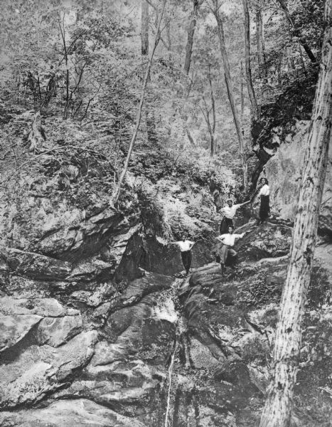 Elevated view of four people posing on a large outcropping of rocks in a wooded area.