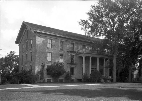 Smith Hall at Ripon College features a three-story porch, supported by columns and which shelters the entrance. Brackets add decoration to the roof. Vines grow up the left side of the brick building.