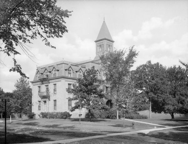View across lawn toward the entrance and side of Bartlett Hall at Ripon College, partially obscured by trees. Decorative stone, wood, and brickwork all ornament the surface of the structure.