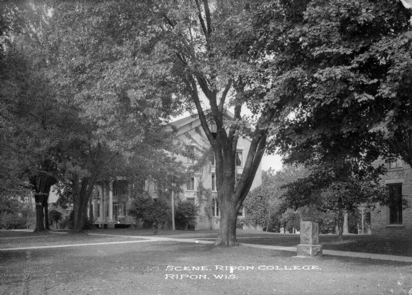 View across lawn toward a campus building at Ripon College. A stone commemorative marker is on the lawn on the right. Caption reads: "Scene, Ripon College, Ripon, Wis."
