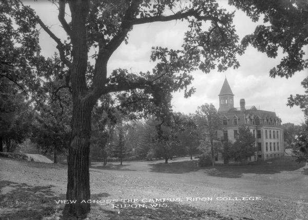 View down hill across lawn toward a three-story building with a cupola at the bottom of the hill on the Ripon College campus. Caption reads: "View across the Campus, Ripon College, Ripon, Wis."