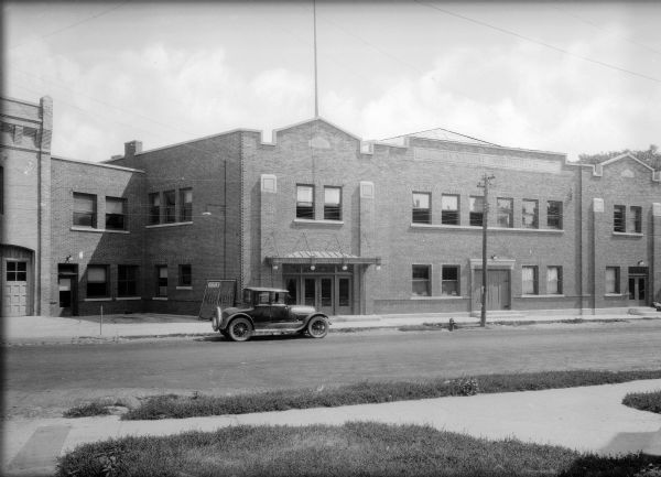 Exterior view of the municipal auditorium, with a car parked along the curb in the street in front of it. Decorative brick and stonework enhance the facade of the structure.