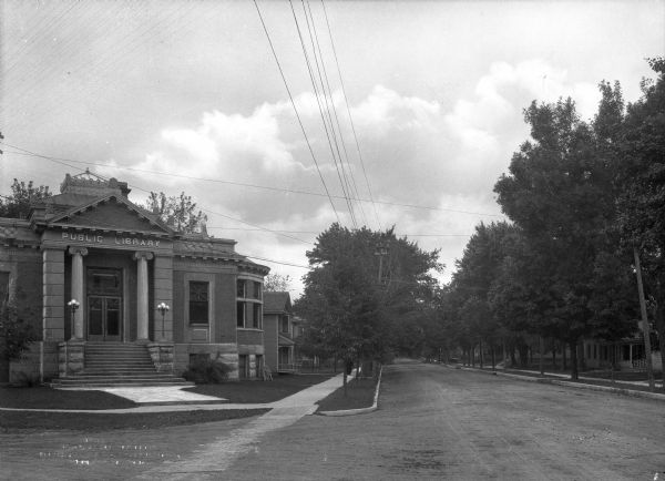 View across intersection toward the library on the left, and houses behind a tree-lined sidewalk on the right.