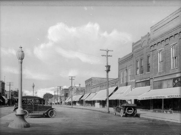 A view of the row of shops along Main Street, with J.W. Allard's store in the foreground on the right. A group of men are further down the street.