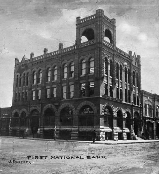 View across intersection toward the First National Bank building on the street corner. The Wausau Business College occupies the third floor, while J.W. Manson Insurance occupies the second floor. Caption reads: "First National Bank."