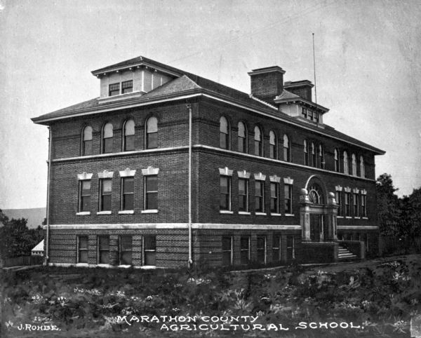 A view of the Marathon County Agricultural School facade. Poured concrete pillars and an arched window surround the entrance.