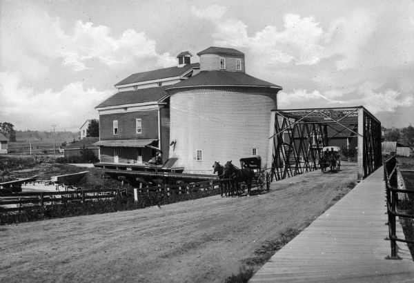 A horse-drawn carriage crosses the Mill Street Bridge while another carriage parks near the grain elevator.