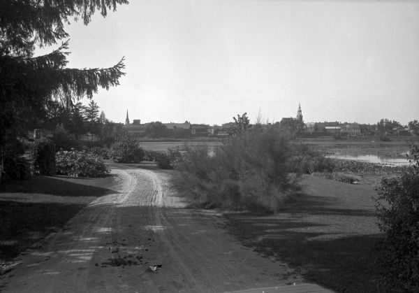 View along a dirt road toward a lake, with the town of Weyauwega on the far shoreline.